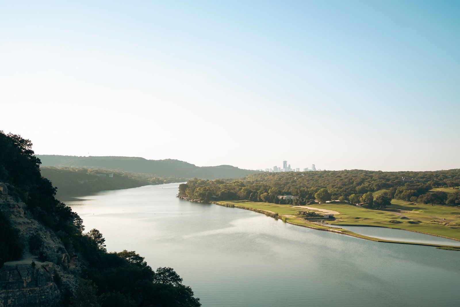 A river winding through trees, eventually leading to downtown Austin in the distance