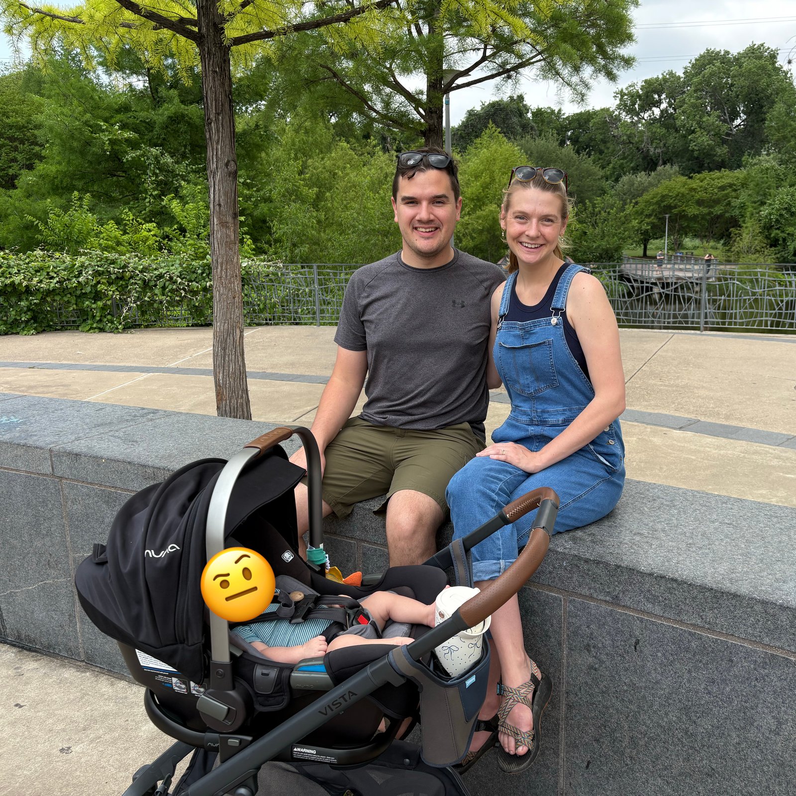 A young couple sitting on a barrier with a newborn baby in a stroller in front of them