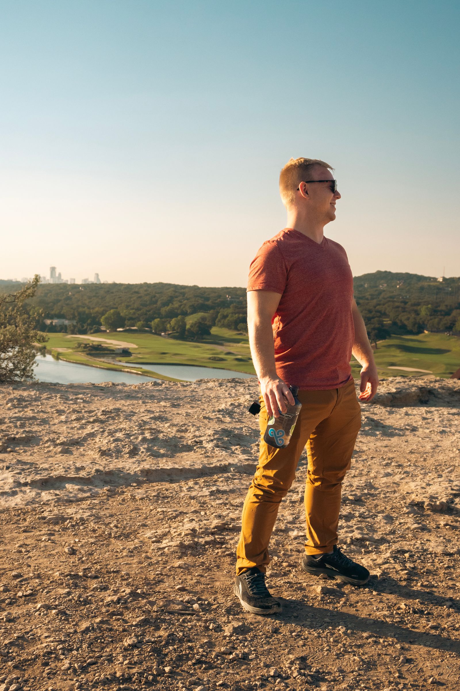 A man standing on a rocky surface in front of the river, with the city in the background