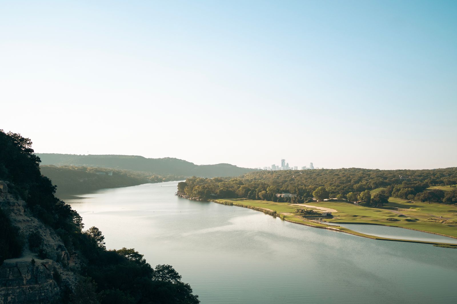 A winding river with trees and greenery on each side, leading to a city in the distance