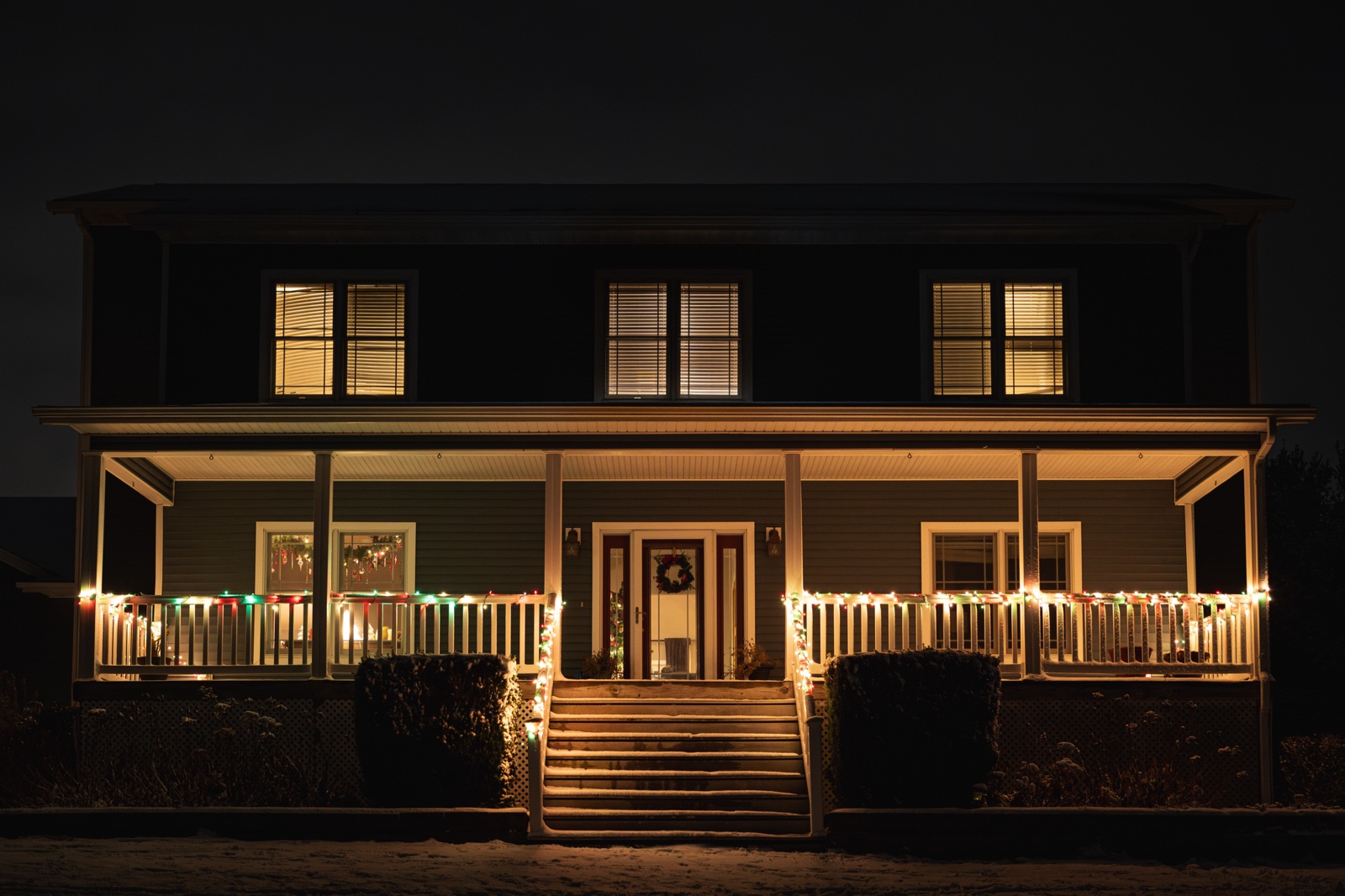 A house in the evening, lit up by Christmas lights on the porch, as well as lights from the inside